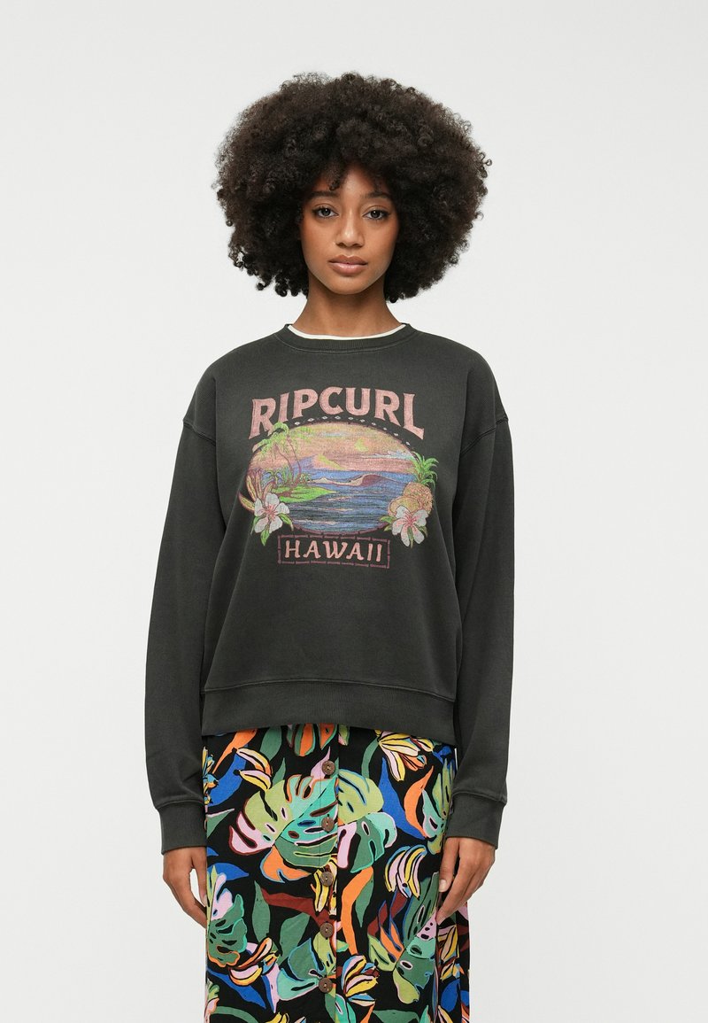 Sweatshirt noir avec un imprimé graphique au style vintage portant l'inscription "Ripcurl Hawaii". Associé à une jupe à motifs floraux multicolores.