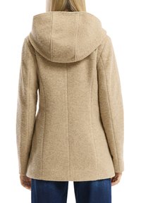 Beige tekstuuriga jakk, millel on suur kapuuts, ümberjooneline lõige ja nähtavad õmbluse detailid, valmistatud pehmest, soonilisest kangast.