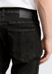 Schwarze Jeans aus Denim mit geradem Schnitt, Gesäßtaschen mit Steppnähten und einem Lederetikett in der Nähe des Bunds.