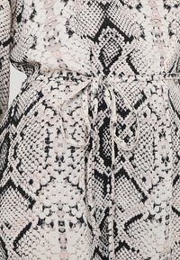 Robe en tissu imprimé serpent avec une fine ceinture nouée à la taille, présentant des motifs géométriques d'écailles en noir, beige et blanc.