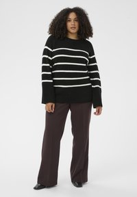 Black and white striped knit sweater with a relaxed fit and long sleeves, paired with dark wide-leg pants. Smooth texture and ribbed hem detail.