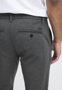 Gray textured trousers with a straight fit, featuring two back pockets, one with a black button, and a woven label on the side.