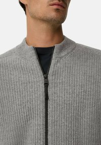 Grauer gerippter Strickpullover mit hohem Kragen und schwarzem Reißverschluss-Detail, der eine glatte Textur und eine figurbetonte Silhouette aufweist.