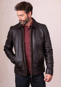 Brown leather jacket with a zipped front, a collared neck, and side pockets, worn over a maroon shirt, displayed against a neutral background.