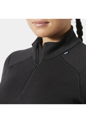 Kobieta w czarnym pulowerze na pół z suwakem, z małym logo "HH" na kołnierzu, widoczna od szyi do klatki piersiowej.