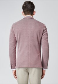 Blazer leggero in tessuto rosa testurizzato con un motivo sottile, vestibilità sartoriale e spacco singolo sul retro. Pantaloni beige chiaro.