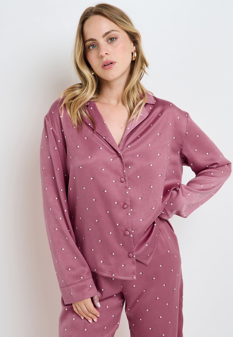Ensemble de pyjama en satin mauve avec de petits motifs de cœurs blancs, comprenant un haut à bouton, des manches longues et un bas assorti.