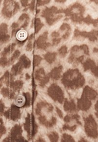 Κοντινό πλάνο καφέ υφάσματος με λεοπάρ σχέδιο, με δύο ραμμένα κουμπιά και ορατή ραφή κατά μήκος της ραφής.