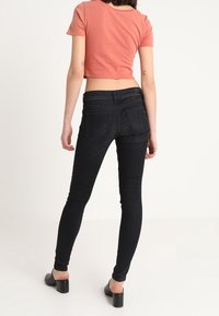 Jeans skinny negros con una cintura alta y dos bolsillos traseros, combinados con una camiseta corta rosa y zapatos de tacón bloque negros.