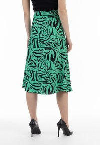 Groene midi-jurk met een zwart abstract patroon, soepele stof, uitlopende ontwerp en een ritssluiting achter. Gecombineerd met zwarte hoge hakken.