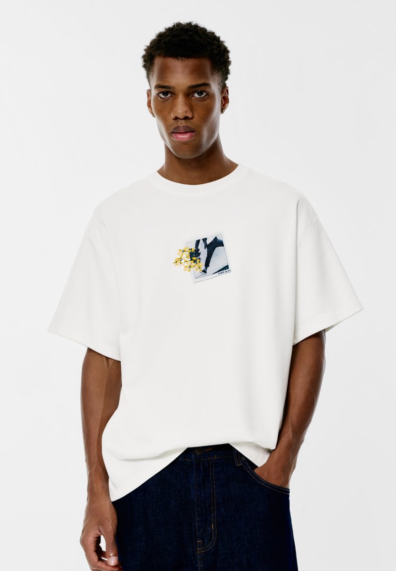 Weißes Baumwoll-T-Shirt mit kurzen Ärmeln, das einen Graf Druck auf der Brust zeigt, der eine Blumenanordnung und abstrakte Formen darstellt.