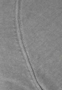 Primo piano di un tessuto grigio chiaro con una cucitura visibile e una texture a maglia fine.