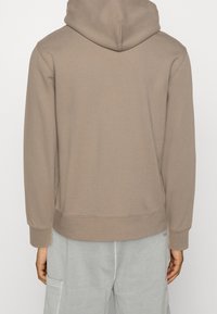 Sweat à capuche taupe, doté d'une poche kangourou, de poignets et d'un ourlet côtelés. Le tissu semble doux avec une texture lisse.