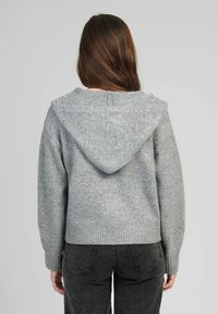 Pull gris avec capuche, fabriqué en matériau tricoté texturé. Dispose d'un ourlet et de poignets côtelés, avec des accents décoratifs près des épaules.