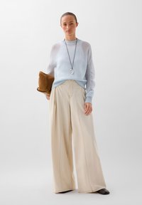 Lichtblauwe gebreide trui, brede beige broek met voorplooien, en een bruine clutch. Lange ketting met ronde hanger.