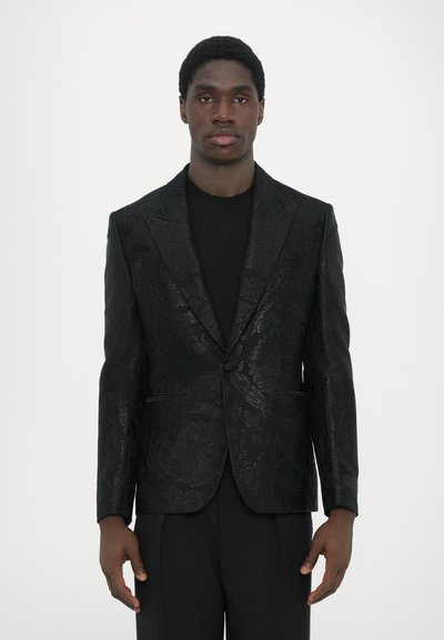Sort mønstret blazer med en blank floral tekstur, enkeltknaplukning og spidse flip, båret over en sort top. Skræddersyet pasform.