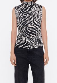 Top senza maniche bianco e nero con collo alto, caratterizzato da un motivo a stampa leopardata vorticoso e tessuto testurizzato. Abbinato a jeans scuri.