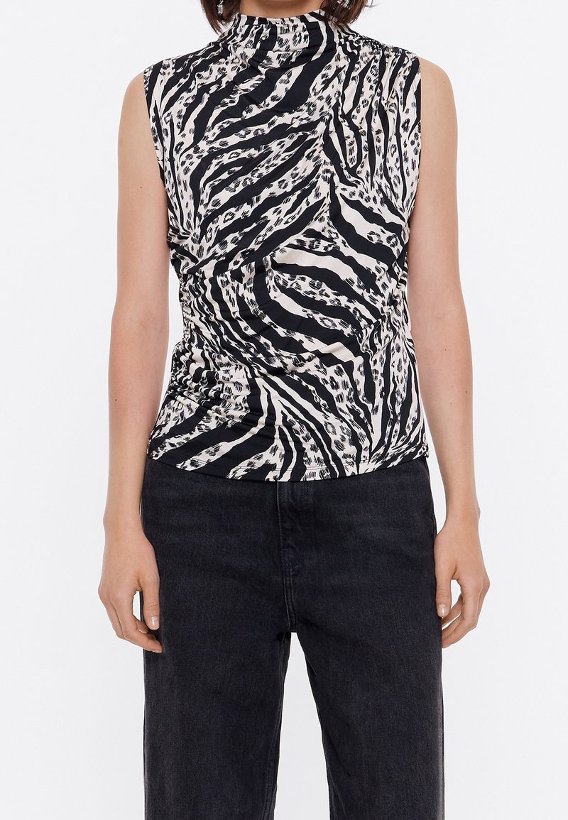 Top senza maniche bianco e nero con collo alto, caratterizzato da un motivo a stampa leopardata vorticoso e tessuto testurizzato. Abbinato a jeans scuri.