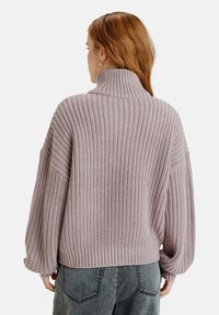 Pull oversized en maille côtelée mauve clair avec un col montant et des épaules tombantes. Texture douce et coupe ample avec des manches larges.