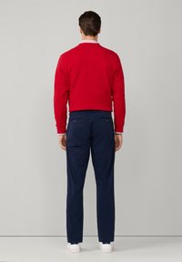 Sudadera roja con cuello redondo, combinada con pantalones azul marino. El conjunto presenta acentos blancos y una textura suave, similar al algodón.