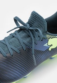 Botas de fútbol con una parte superior textil de color azul oscuro y un patrón de puntos, logo de color verde brillante y cordones planos. Acentuadas con rayas de color azul claro.