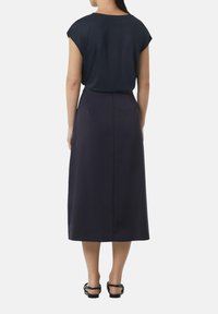 Granatowa bluzka na krótkim rękawie w połączeniu z luźną, długą do kostek ciemną spódnicą. Gładka faktura, minimalistyczny design, a całość dopełniają płaskie sandały.