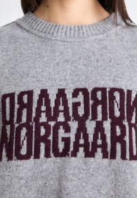 Maglione grigio a maglia con collo rotondo a coste e design testuale di un mogano scuro. La texture è morbida e il motivo presenta lettere alternate.