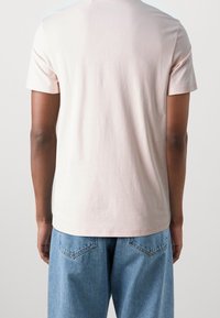 Camiseta de algodón de color rosa claro con mangas cortas, corte recto y cuello redondo, combinada con unos pantalones vaqueros de denim azul de corte holgado.