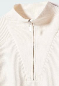 Cremfarbener, gerippter Strickpullover mit silbernem Reißverschluss und Stehkragen.