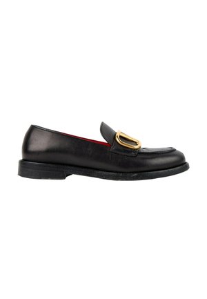 Mocassin en cuir noir avec un petit talon et une boucle métallique dorée sur le dessus avant, présenté en profil latéral sur fond blanc.