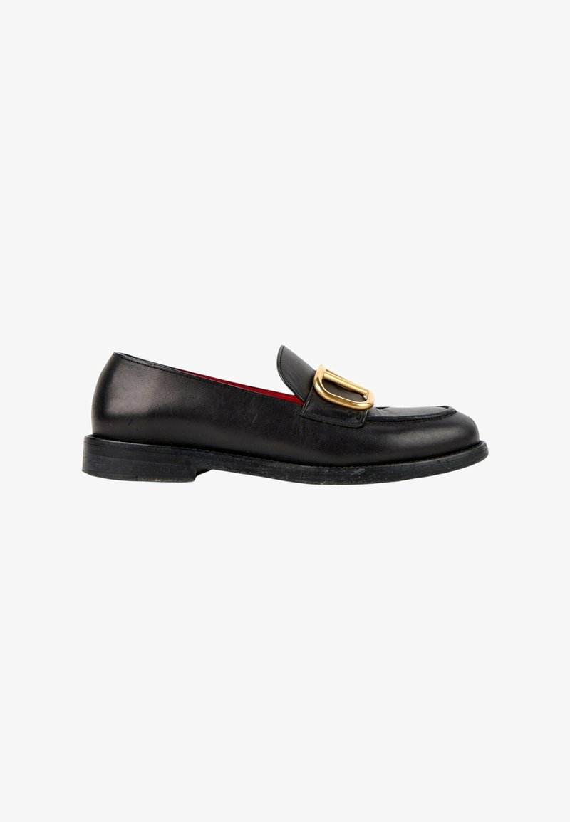 Mocassin en cuir noir avec un petit talon et une boucle métallique dorée sur le dessus avant, présenté en profil latéral sur fond blanc.