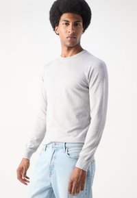 Light grey long-sleeve sweater made of a smooth knit fabric, featuring a round neckline and fitted cuffs, paired with light blue jeans.