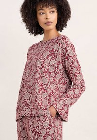 Top con patrón floral en color burdeos, de mangas largas y cuello redondo, hecho de una tela ligera. Presenta intrincados diseños florales en blanco y un corte holgado.