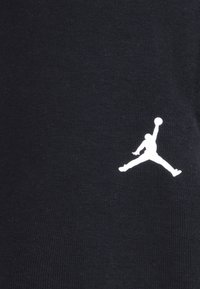 Tela negra con una textura suave que presenta un logo Jumpman en blanco. El logo representa una figura en pleno salto, sosteniendo un balón de baloncesto.