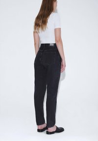 Schwarze Jeans aus Denim mit legerem Schnitt, hoher Taille und kontrastierenden Nähten. Die Rückansicht zeigt zwei Taschen und ein Markenetikett am Bund.