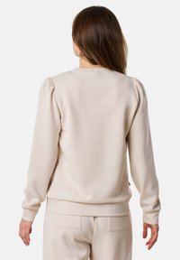 Felpa beige con collo tondo, dettagli a spalle montate e polsini a costine. Tessuto dalla texture liscia con una vestibilità morbida.