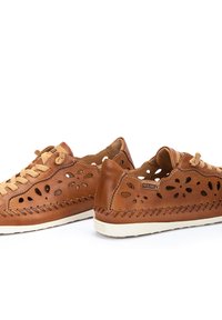 Chaussures en cuir marron avec des découpes florales, bout rond, lacées à l'avant, et couture contrastante le long de la semelle. Semelle extérieure en caoutchouc blanc.
