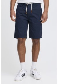 Navy blue cotton shorts with a drawstring waist, front pockets, and cuffed hems, paired with white sneakers and ribbed socks.