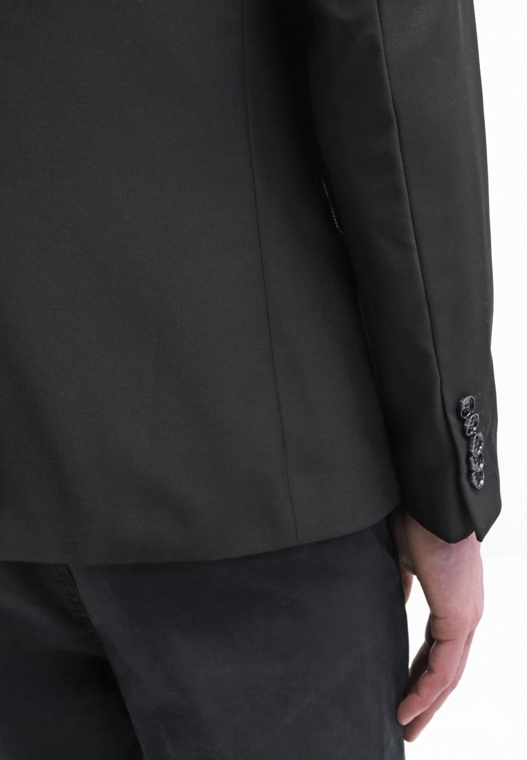 Svart blazer med strukturerad tyg, slim fit och treknappsknappade manschetter. Materialet har en slät textur med en matt finish.