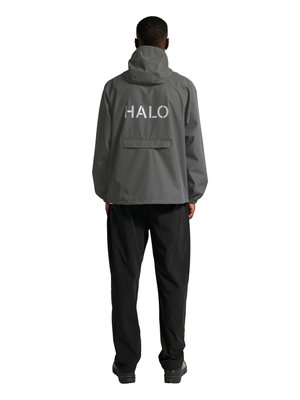 Mann trägt graue Kapuzenjacke mit der Aufschrift "HALO" auf dem Rücken, kombiniert mit schwarzen Hosen und schwarzen Schuhen, steht mit dem Rücken zum Betrachter auf weißem Hintergrund.