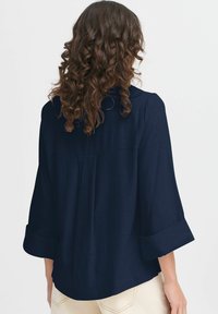 Blusa blu navy con una vestibilità comoda, maniche a tre quarti, tessuto strutturato e polsini arrotolati. Presenta una piega sul retro per una forma aggiuntiva.