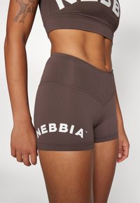 Smešane sportske kratke hlače smeđe boje s visokim strukom, s bijelim "NEBBIA" logotipom. Glatki materijal i prilagođen dizajn idealni za vježbanje.