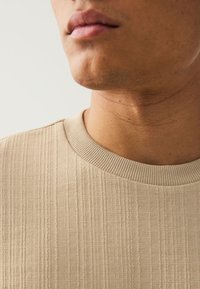 Beige cotton sweater with ribbed texture, round neckline, and smooth finish, showcasing a close-up of the fabric and collar details.