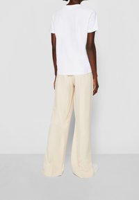 White cotton short-sleeve t-shirt paired with loose-fitting, light beige wide-leg trousers, viewed from the back. Simple design, no patterns.