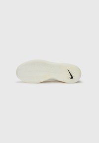 Semelle de sneaker blanche avec une surface texturée et un logo Nike swoosh noir. Présente un motif de semelle ondulé pour l'adhérence et la stabilité.