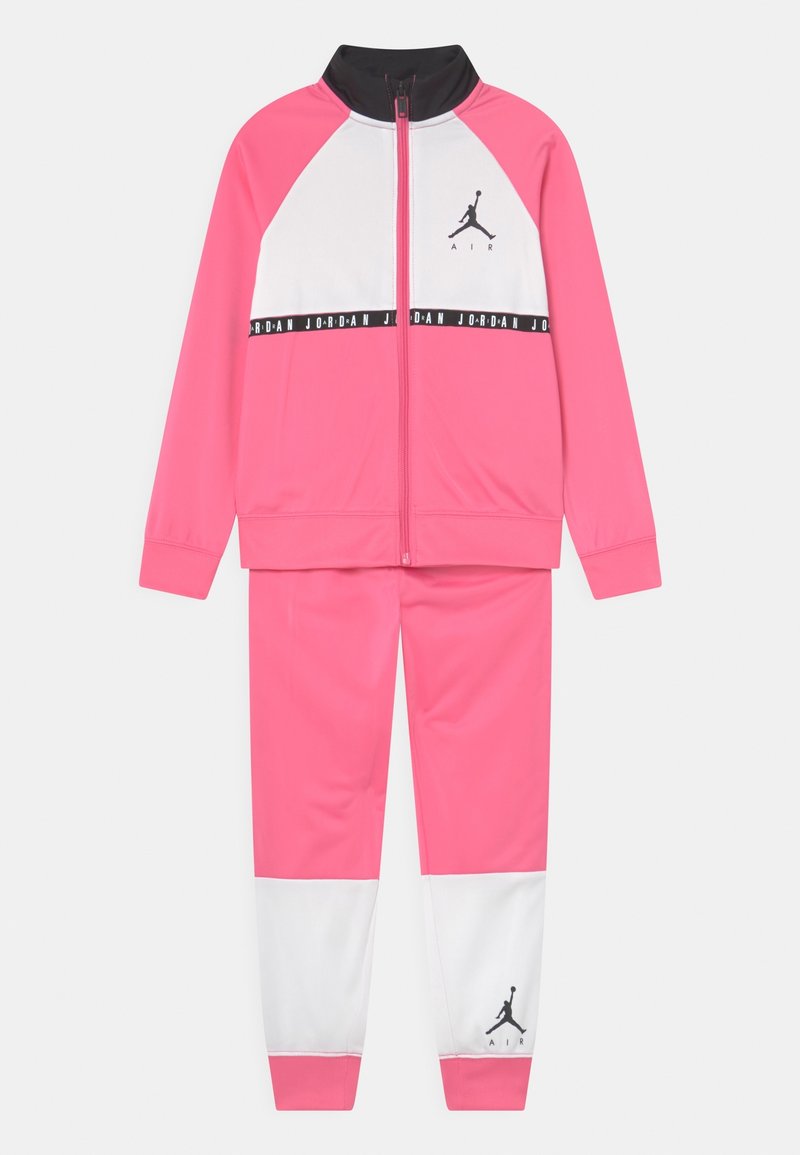 Survêtement Jordan rose et blanc avec col noir, veste zippée intégrale, logo sur la poitrine et le pantalon, et bande avec le texte « Jordan » sur la poitrine.