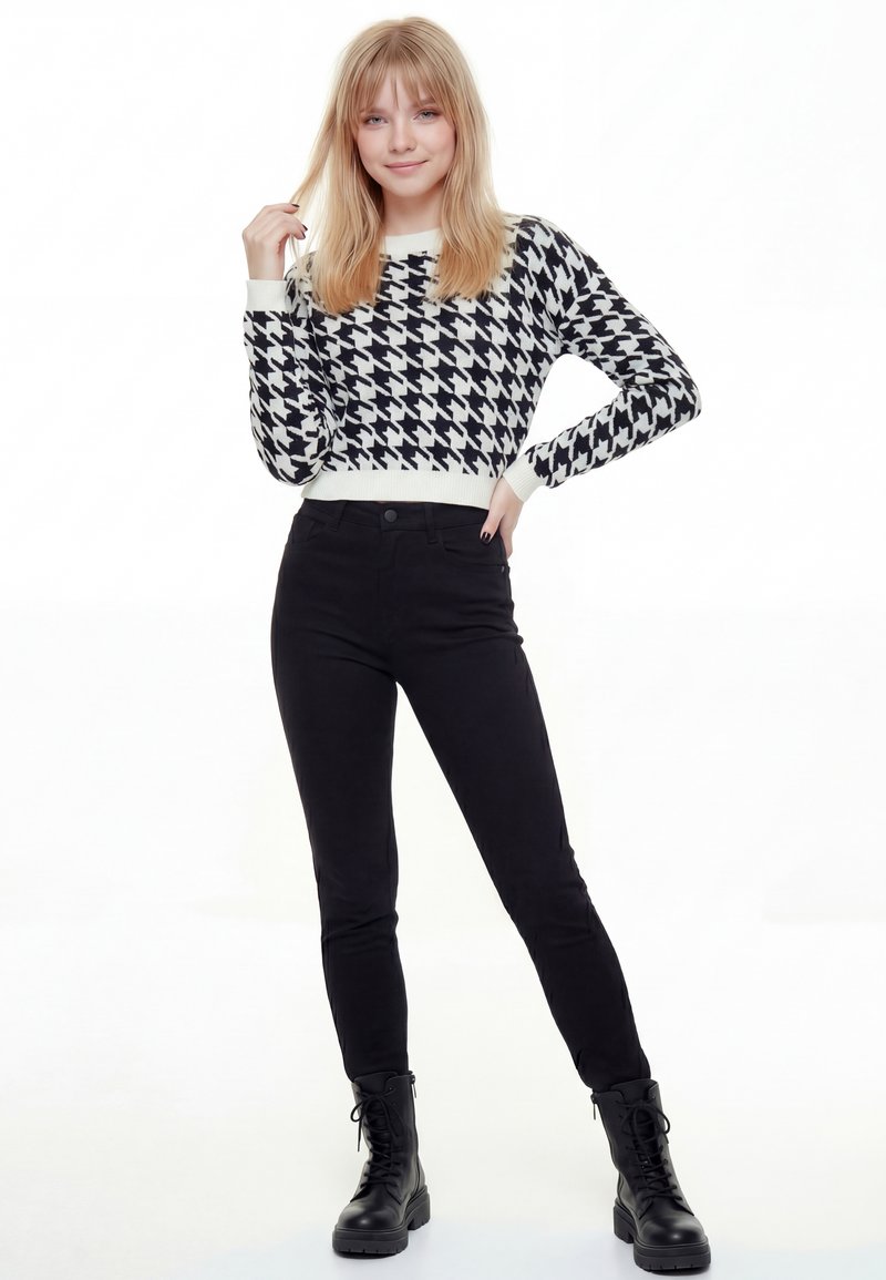 Pull noir et blanc à motif pied-de-poule avec un col côtelé, porté avec un pantalon noir taille haute et des bottes noires à lacets.
