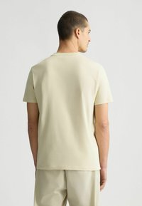 Hellbeige kurzärmliges T-Shirt aus weichem, glattem Stoff. Verfügt über einen klassischen Rundhalsausschnitt und ein schlichtes, minimalistisches Design.