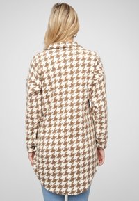 Cămașă lungă din fleece tartan, în dungi maro și crem cu model houndstooth, având guler, mâneci lungi și un tiv rotund.