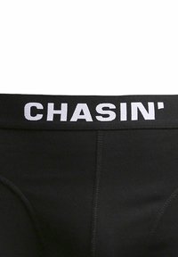Biancheria intima nera con una cintura elastica recante la scritta "CHASIN'" in grassetto bianco. Il tessuto appare liscio con un design aderente.